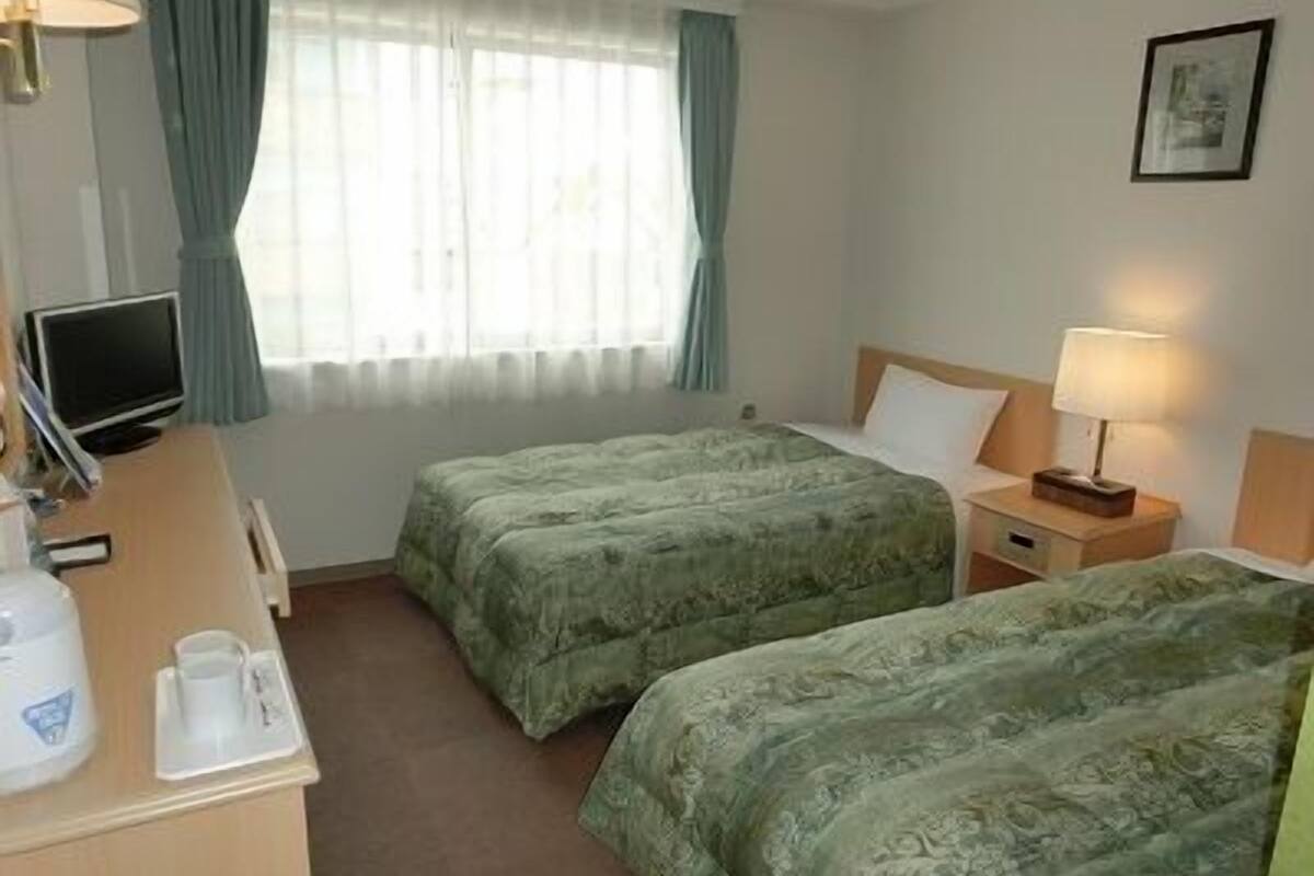 A hotel room with two beds, a desk with a computer, a coffee maker, and a window with curtains.