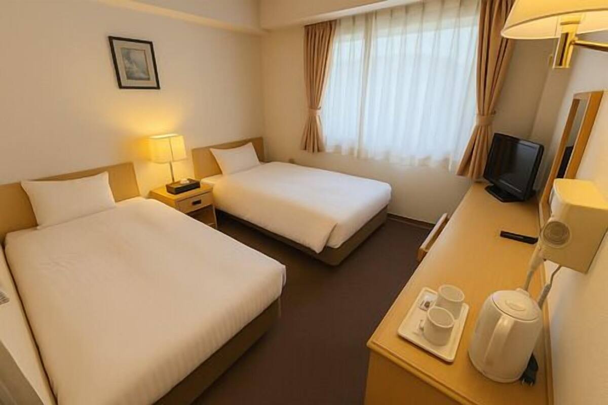 A hotel room with two beds, a desk with a TV, a coffee maker, and a window with curtains.