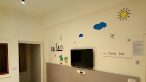 A room with a television mounted on the wall, a door, and a wall with stickers depicting a sun, clouds, and a bee. - Fu Xing Homestay (Magong)
