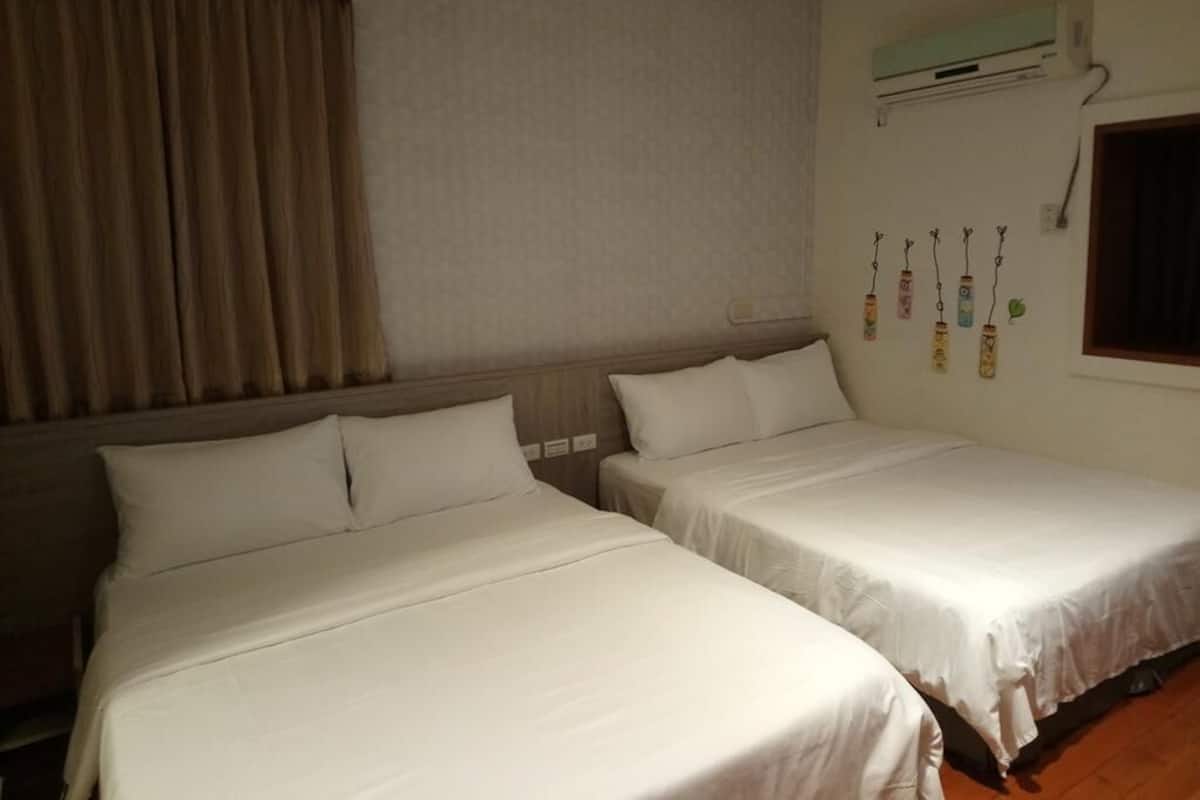 A hotel room with two beds, a window, and a wall-mounted air conditioner.