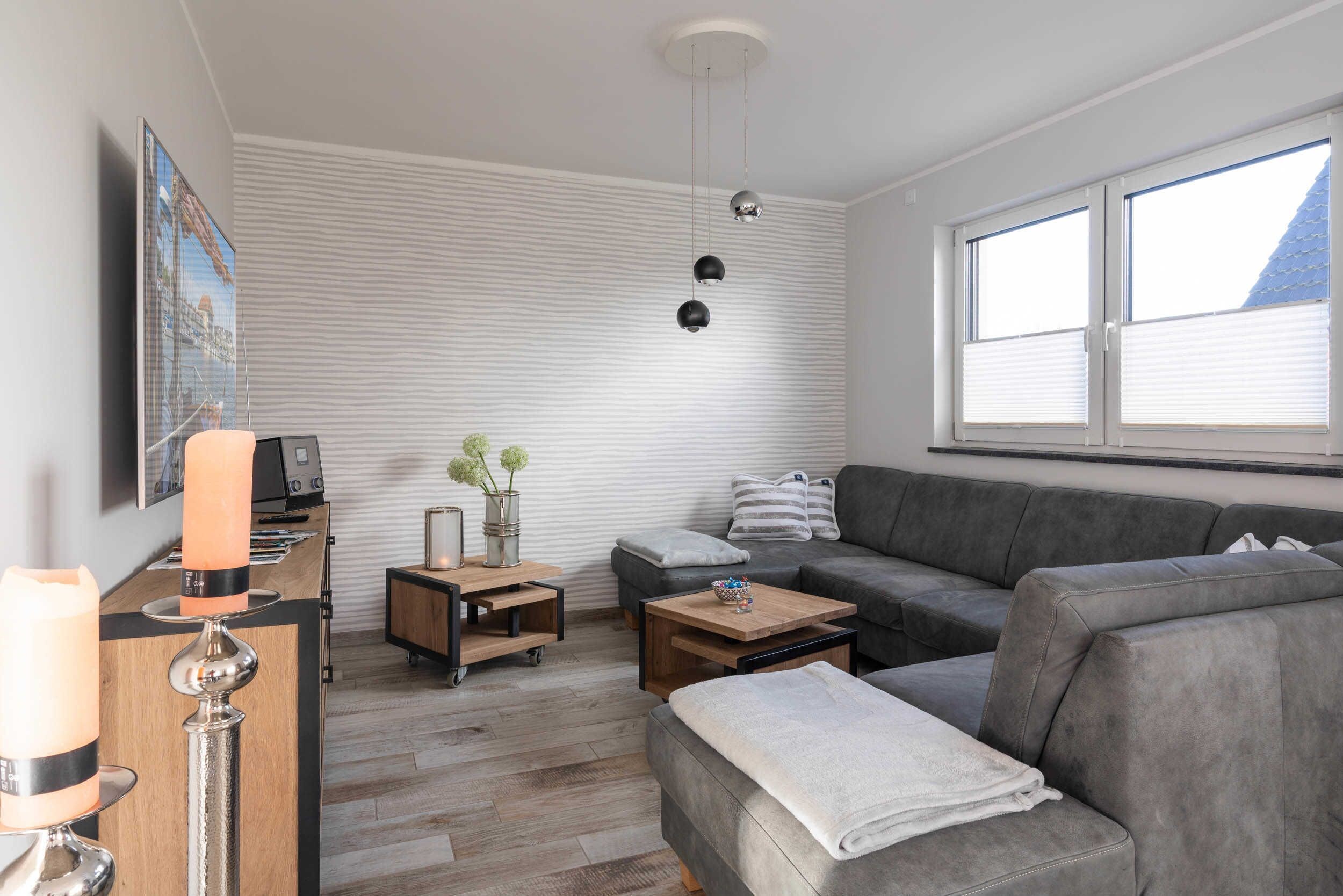 Un salon moderne avec un canapé gris, une table basse en bois, un téléviseur posé sur un meuble et une lampe fixée au mur.