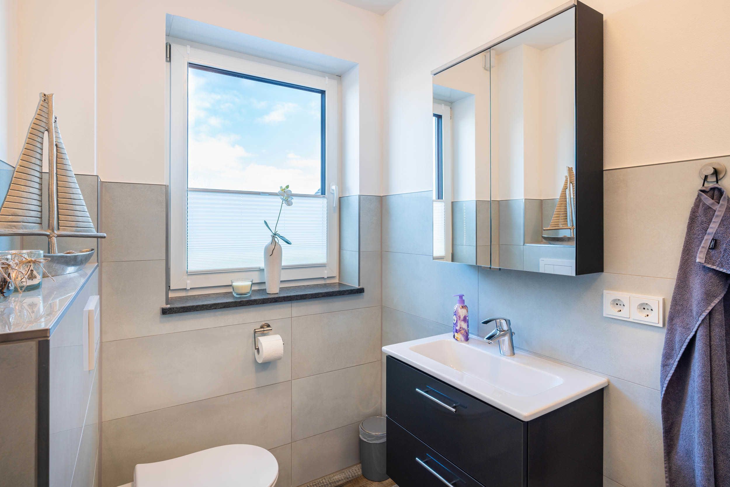 A bathroom with a window, a sink, a mirror, and a toilet.