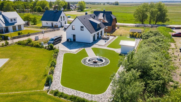 Een woonwijk met een centraal gelegen wit huis, een gazon in een cirkelvormig ontwerp en veel groen eromheen.