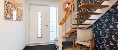 A staircase with wooden steps and a chair, a door with a doormat, and a wall with a nautical-themed wallpaper.