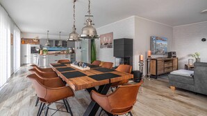 Een moderne keuken met een eetgedeelte, met een grote houten tafel, bruine leren stoelen, hanglampen en een uitzicht op de keuken op de achtergrond.