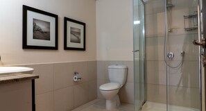 A bathroom with a toilet, a sink, and a glass-enclosed shower. There are two framed pictures on the wall. - Villa TD02 TV - Arethusa (Kouklia)