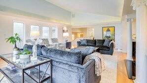 Ein geräumiges Wohnzimmer mit einem großen grauen Sofa, einem Glastisch und einem Essbereich mit modernem Tisch und Stühlen.