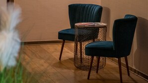 A hallway with a wooden floor, a blue chair, a round table, and wall-mounted artwork. - Hotel Beau Rivage (Aix-les-Bains)