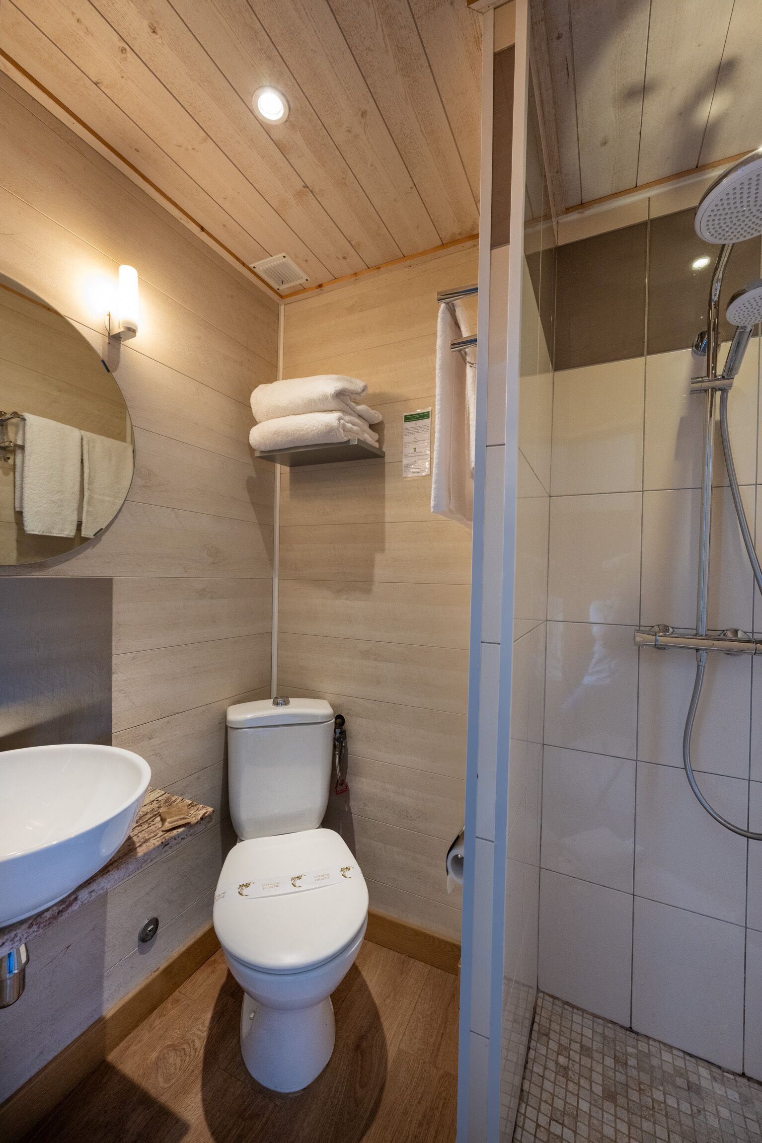 A bathroom with a wooden ceiling, a white toilet, a sink, and a shower area.