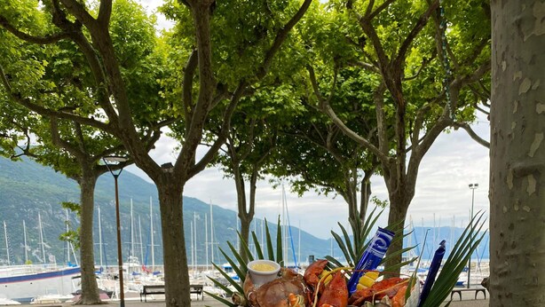 A table set for a meal with seafood, wine glasses, and a view of boats and trees. - Hotel Beau Rivage (Aix-les-Bains)