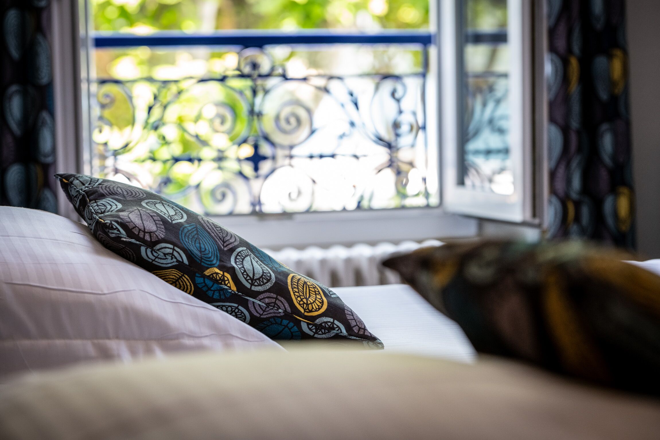 A bed with patterned pillows and a view of a balcony with ornate metal railings.
