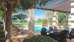 Eine überdachte Terrasse mit Pool, Sitzgelegenheiten im Freien und einer Steinpfeiler.