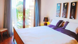 Ein Schlafzimmer mit einem Bett, einem Sessel, einem Nachttisch und einem Fenster mit Vorhängen.