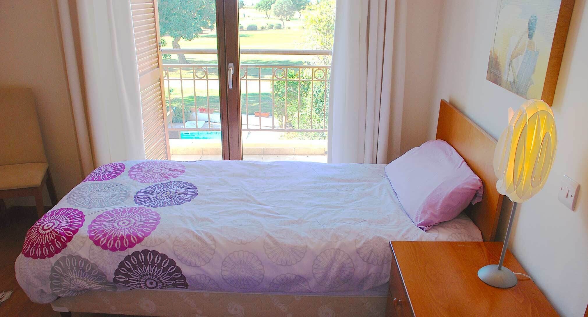 A bedroom with a bed, a nightstand, a wall-mounted fan, and a balcony view.