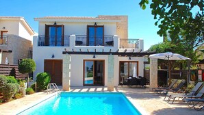 Ein zweistöckiges Haus mit Schwimmbad, Außenmöbeln und einer Pergola.