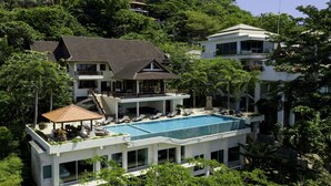 A multi-story resort with a large swimming pool, multiple balconies, and lush greenery surrounding the property.