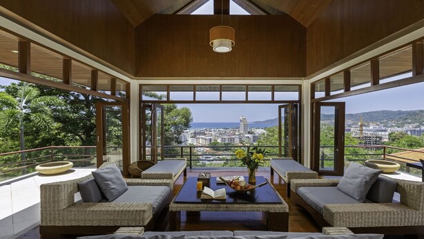 A spacious balcony with wicker furniture, a coffee table with a vase, and a view of the city and sea.