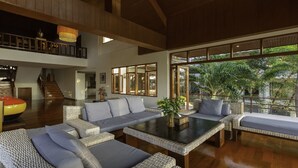 A spacious living area with a large window, wicker furniture, and a staircase leading to an upper level.