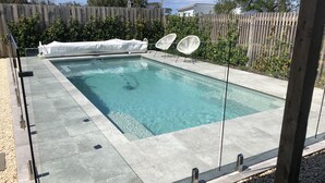 A rectangular swimming pool with clear water, surrounded by a tiled deck and a wooden fence. - Torquay - SpringHaven Beach House (Torquay)