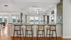 Une cuisine moderne dotée d’un îlot central, de tabourets de bar et offrant une vue sur l’extérieur.