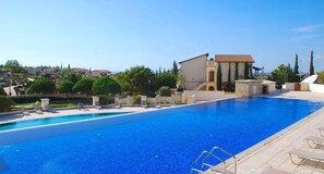 A large swimming pool with lounge chairs and a stone wall. - Villa Kallithea - APR04 (Kouklia)