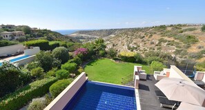 A rooftop pool with a view of a green lawn and distant hills. - Villa Kallithea - APR04 (Kouklia)