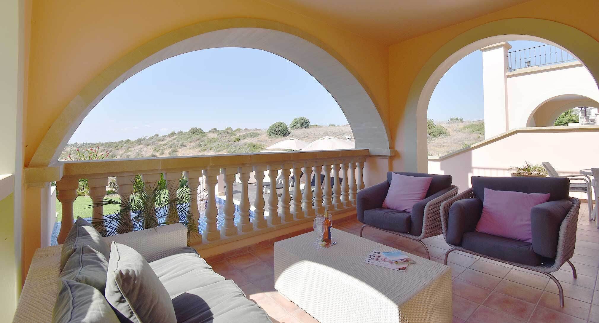 A covered outdoor seating area with two sofas, a small table, and a view of the landscape.