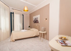 Une chambre bien rangée, avec un lit, une table de chevet et une petite table ronde sur laquelle repose un magazine.