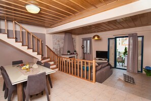 A spacious living area with a wooden staircase, a dining table with chairs, a sofa, and a television.