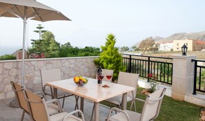 Une table avec une bouteille de vin et des verres, entourée de chaises, avec un mur de pierre et, en arrière-plan, une vue sur la verdure et des bâtiments.