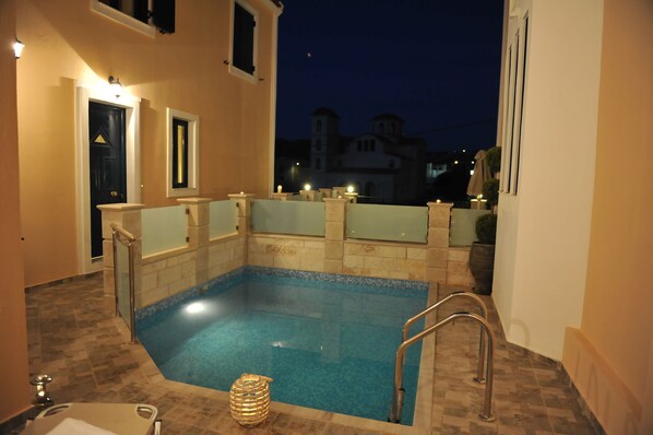 Une piscine avec une terrasse carrelée, un petit espace salon et une vue sur les bâtiments en arrière-plan.