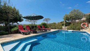 A swimming pool with red lounge chairs and a green umbrella. - Villa HG01 - Madelini (Kouklia)