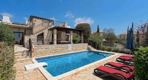A swimming pool with stone walls, a staircase leading to a covered area, and red lounge chairs. - Villa HG01 - Madelini (Kouklia)