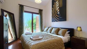 A hotel room with a large bed, a nightstand, a lamp, and a painting on the wall. - Villa HG01 - Madelini (Kouklia)