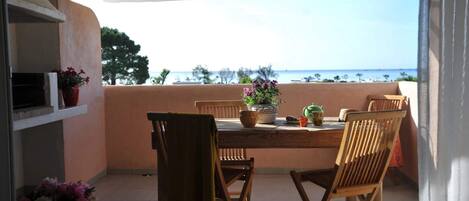 A balcony with a wooden table and chairs, overlooking a beach.