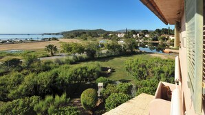 Une vue depuis un balcon donnant sur une zone côtière, avec un ciel dégagé, un champ herbeux et une étendue d'eau à l'horizon.