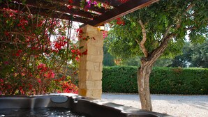 A hot tub under a pergola with stone pillars, surrounded by lush greenery and flowering plants. - Villa 81 - Paparouna (Kouklia)