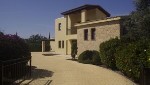 A two-story house with a stone facade, a balcony, and a paved driveway. - Villa 81 - Paparouna (Kouklia)