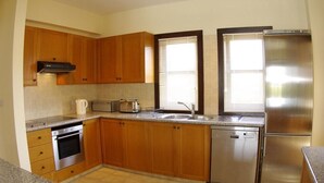A modern kitchen with wooden cabinets, stainless steel appliances, a built-in oven, and a dishwasher. - Villa 81 - Paparouna (Kouklia)