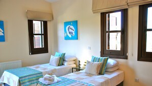 A room with two beds, each with a striped bedspread and pillows, a radiator, a painting on the wall, and windows with blinds. - Villa 81 - Paparouna (Kouklia)