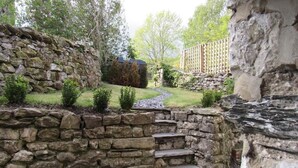A stone staircase leading up to a wooden deck, surrounded by a stone wall and greenery.