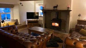 A cozy living room with a fireplace, leather sofas, a television, and a wooden ceiling.