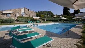 Ein Pool mit Liegestühlen, ein Steinhaus und ein klarer Himmel.