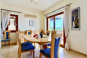 Un comedor con una mesa redonda de madera, sillas tapizadas en azul y vistas al exterior a través de amplias ventanas.