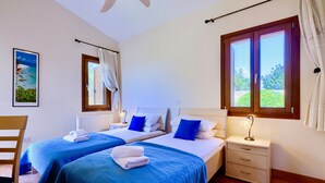 A room with two beds, a chair, a nightstand, a window, and a painting on the wall. - Villa 98 - Helidoni (Kouklia)