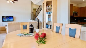 A dining area with a wooden table, chairs, a ceiling fan, a bookshelf, and a kitchen in the background. - Villa 98 - Helidoni (Kouklia)