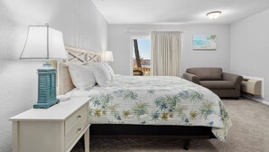 Un dormitorio con cama, una silla, una mesita de noche, una lámpara y una ventana con cortinas.