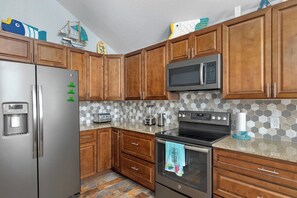 A kitchen with wooden cabinets, stainless steel appliances, a microwave, a toaster, and a patterned backsplash. - Deja Blue - Three Bedroom House, Sleeps 12 (Osage Beach)