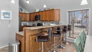 Una cocina moderna con armarios de madera, una isla central con taburetes de bar, un microondas y un refrigerador de acero inoxidable.