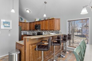A modern kitchen with wooden cabinets, a central island with bar stools, a microwave, and a stainless steel refrigerator.